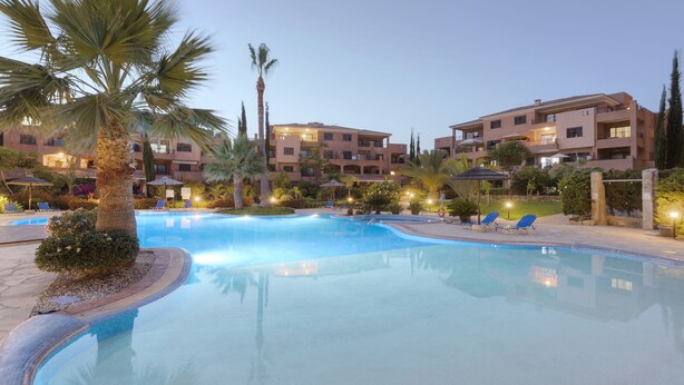 A hotel with a swimming pool, palm trees, and lounge chairs. - Resitour - Aphrodite Gardens (Paphos)