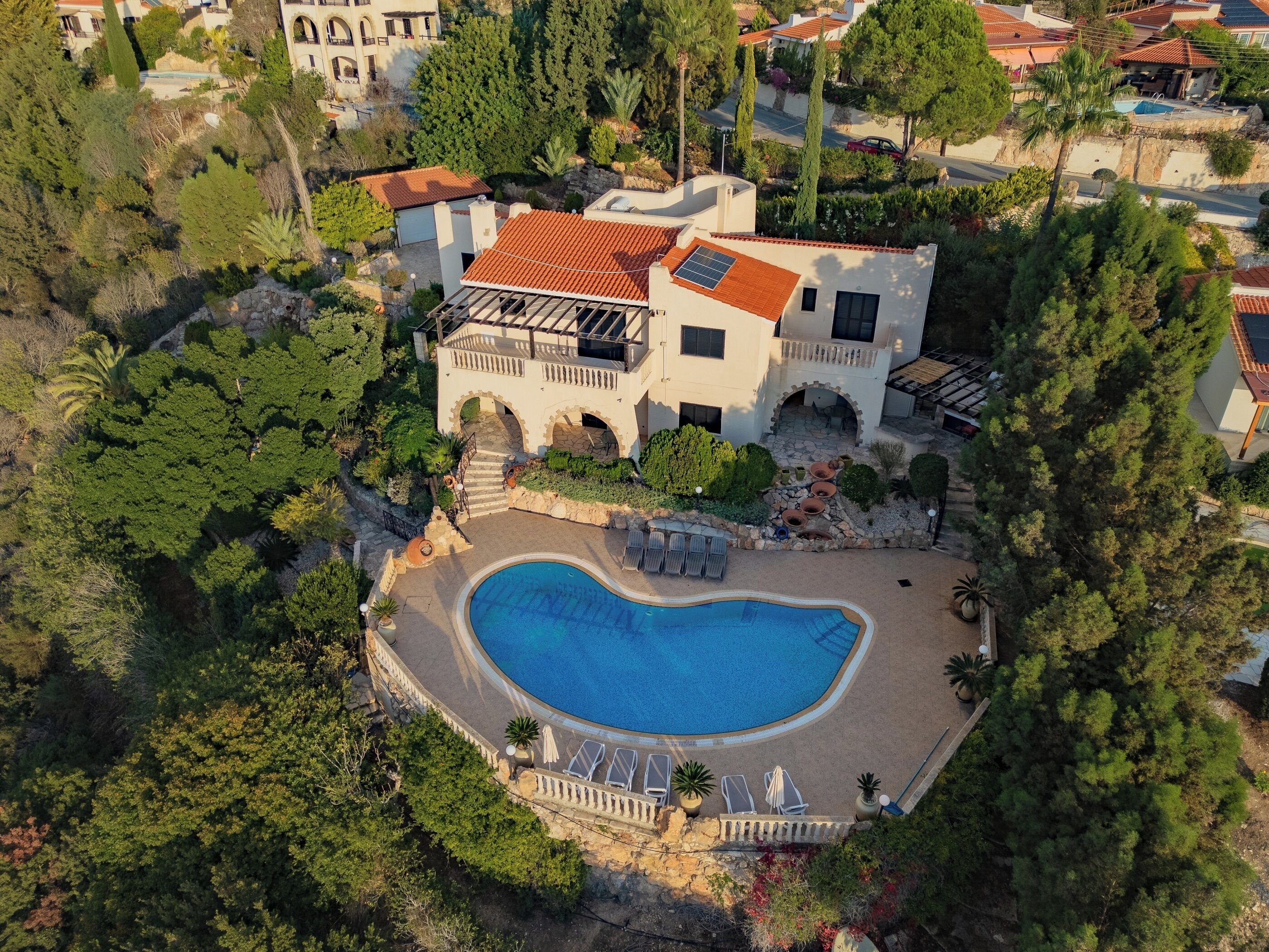 A large house with a swimming pool, surrounded by trees and a garden.