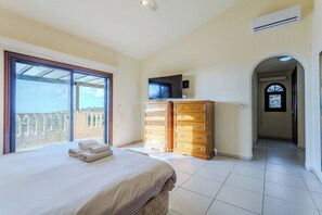 A bedroom with a bed, a TV, a wooden dresser, and a balcony with a view.