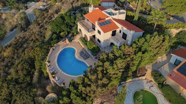 An aerial view of a villa with a swimming pool, surrounded by dense trees and a hilly landscape. - Resitour - Kamares Village (Tala)