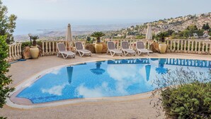 A pool with lounge chairs and umbrellas, surrounded by a stone wall and potted plants. - Resitour - Kamares Village (Tala)