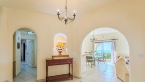 A spacious interior with a chandelier, a wooden console table, and a view of the outdoors through an arched doorway. - Resitour - Kamares Village (Tala)
