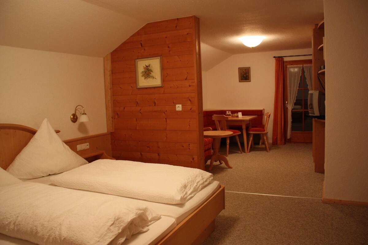 A bedroom with a wooden headboard, a bed with white linens, a small table with chairs, and a television in the corner.