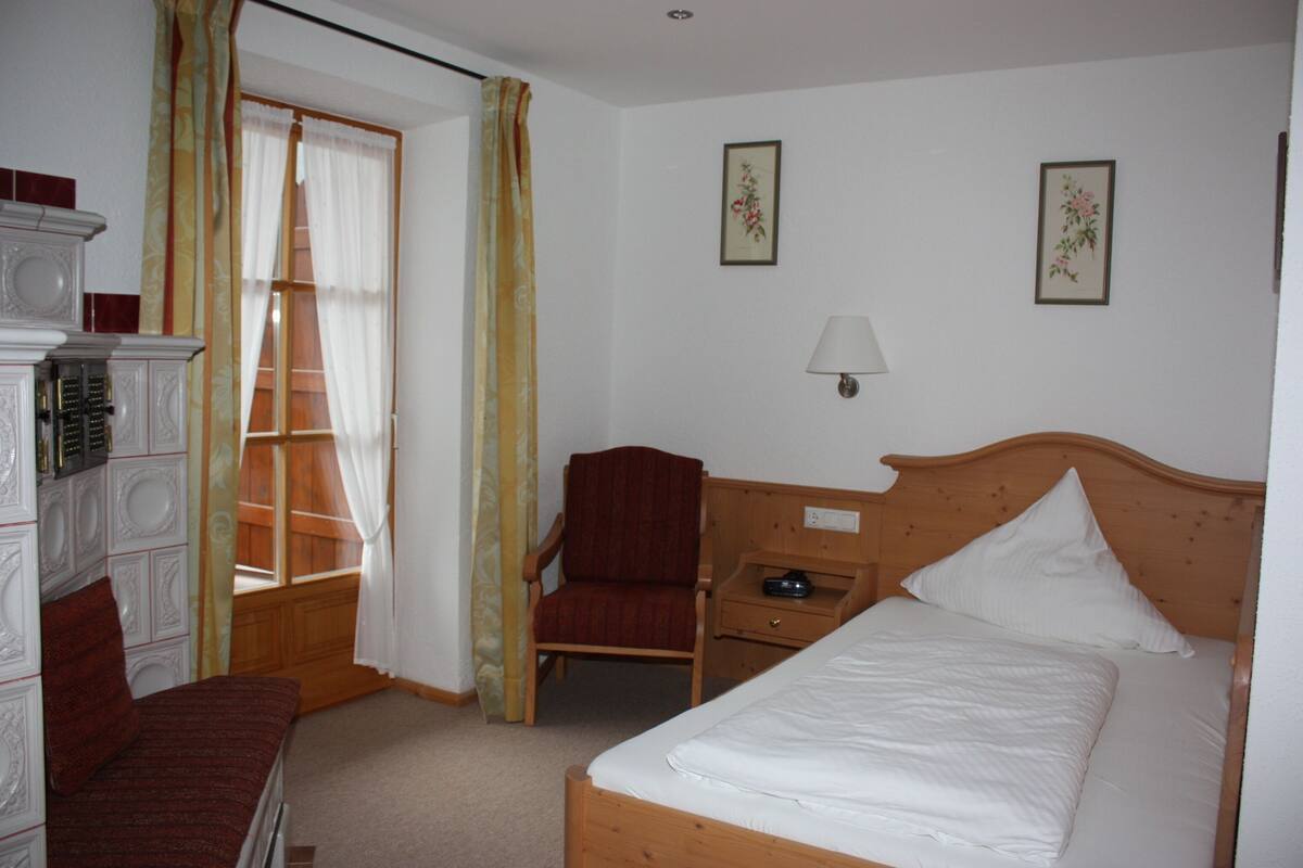 A hotel room with a bed, a chair, a desk, a lamp, and a wardrobe.