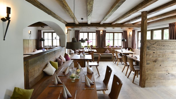 Un comedor rústico con mesas y bancos de madera, ventanas amplias y vigas de madera a la vista en el techo.