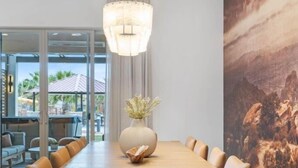 A modern dining area with a long wooden table, beige chairs, a central vase with dried flowers, and a large landscape mural on the wall. - Premier Poolside Location | Private Hot Tub + Fire Pit | Ping Pong | Arcadia #13 (Santa Clara)