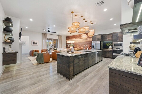 Una cocina moderna con una isla central, armarios de madera oscura, electrodomésticos de acero inoxidable e iluminación colgante.