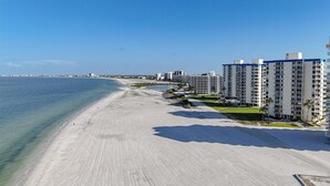 Um hotel à beira-mar com uma extensa praia de areia, águas azuis cristalinas e edifícios altos ao fundo.