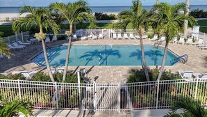 Área de piscina com espreguiçadeiras e palmeiras, cercada por um muro branco.