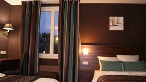 A hotel room with two beds, a window with curtains, a wall-mounted lamp, and a painting on the wall. - Hotel Le Montloire (Montlouis-sur-Loire)