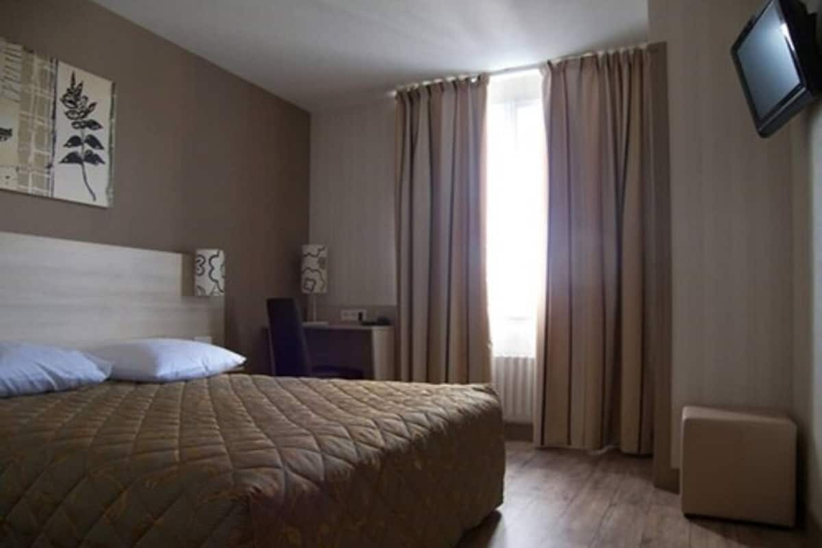 Habitación de hotel con una cama grande, un escritorio, una silla, un televisor y cortinas.