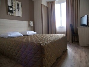 Una habitación de hotel con cama, televisión y ventana con cortinas.