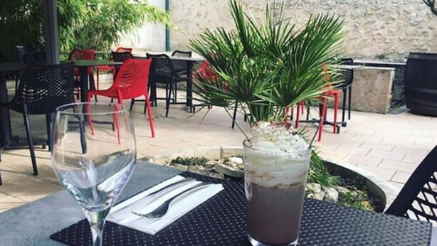 An outdoor seating area with tables and chairs, a potted plant, and a glass of iced beverage. - Hotel Le Montloire (Montlouis-sur-Loire)