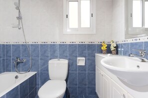 A bathroom with a bathtub, toilet, and sink, featuring blue tiles and a window above the toilet. - Resitour - Limnaria Gardens (Paphos)