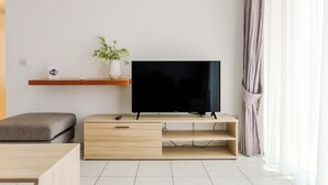 Un salon moderne avec un téléviseur à écran plat, un meuble TV en bois, un canapé gris, une petite table et une plante.