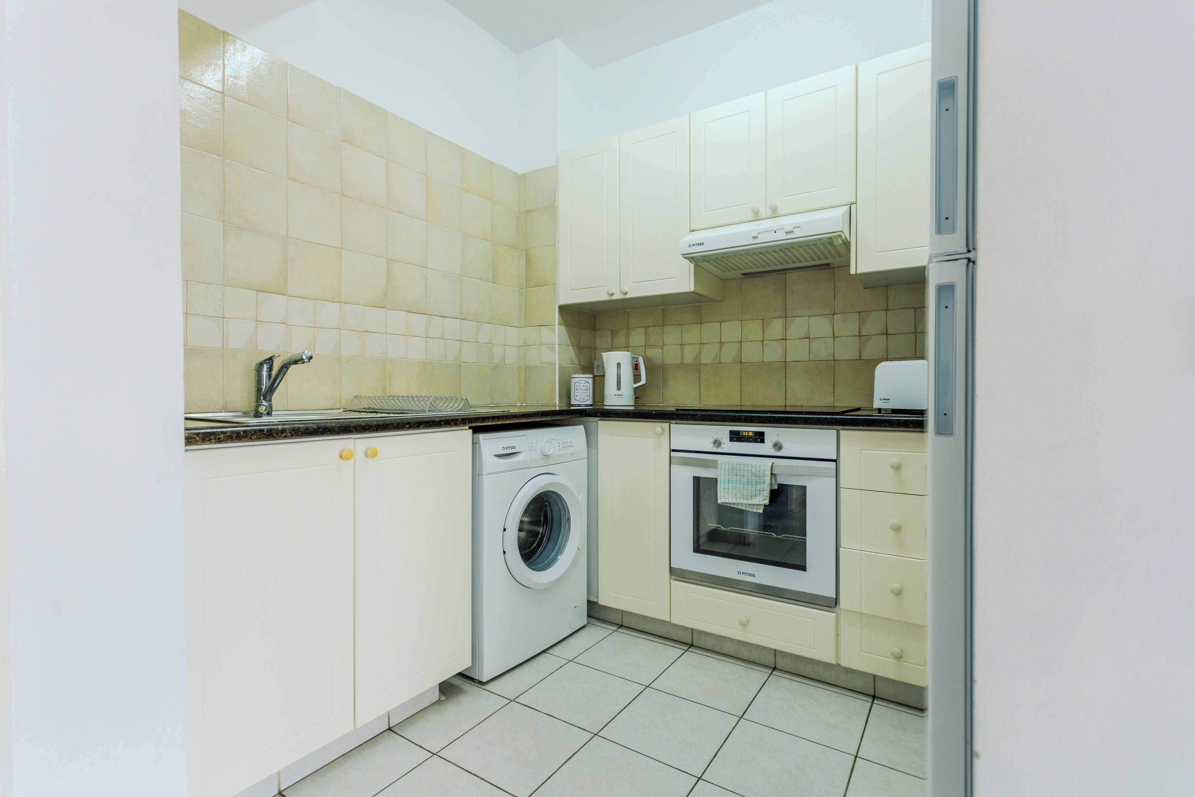 A compact kitchen with a washing machine, oven, and a coffee maker.