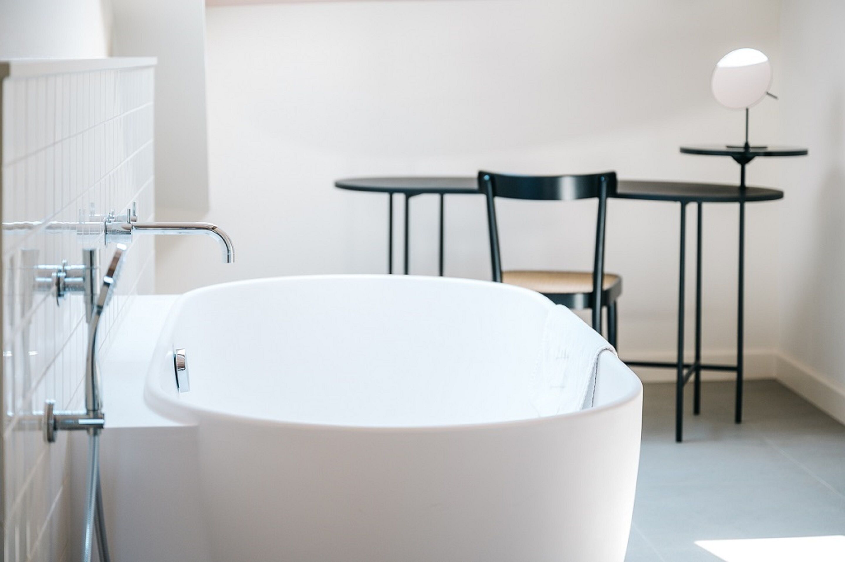 Une salle de bain moderne avec une baignoire sur pieds, une petite table ronde et une chaise.