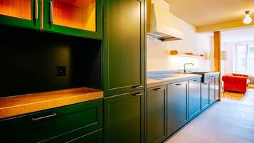 Una cocina moderna con armarios verdes, una encimera de madera y un sofá rojo en la zona de estar.