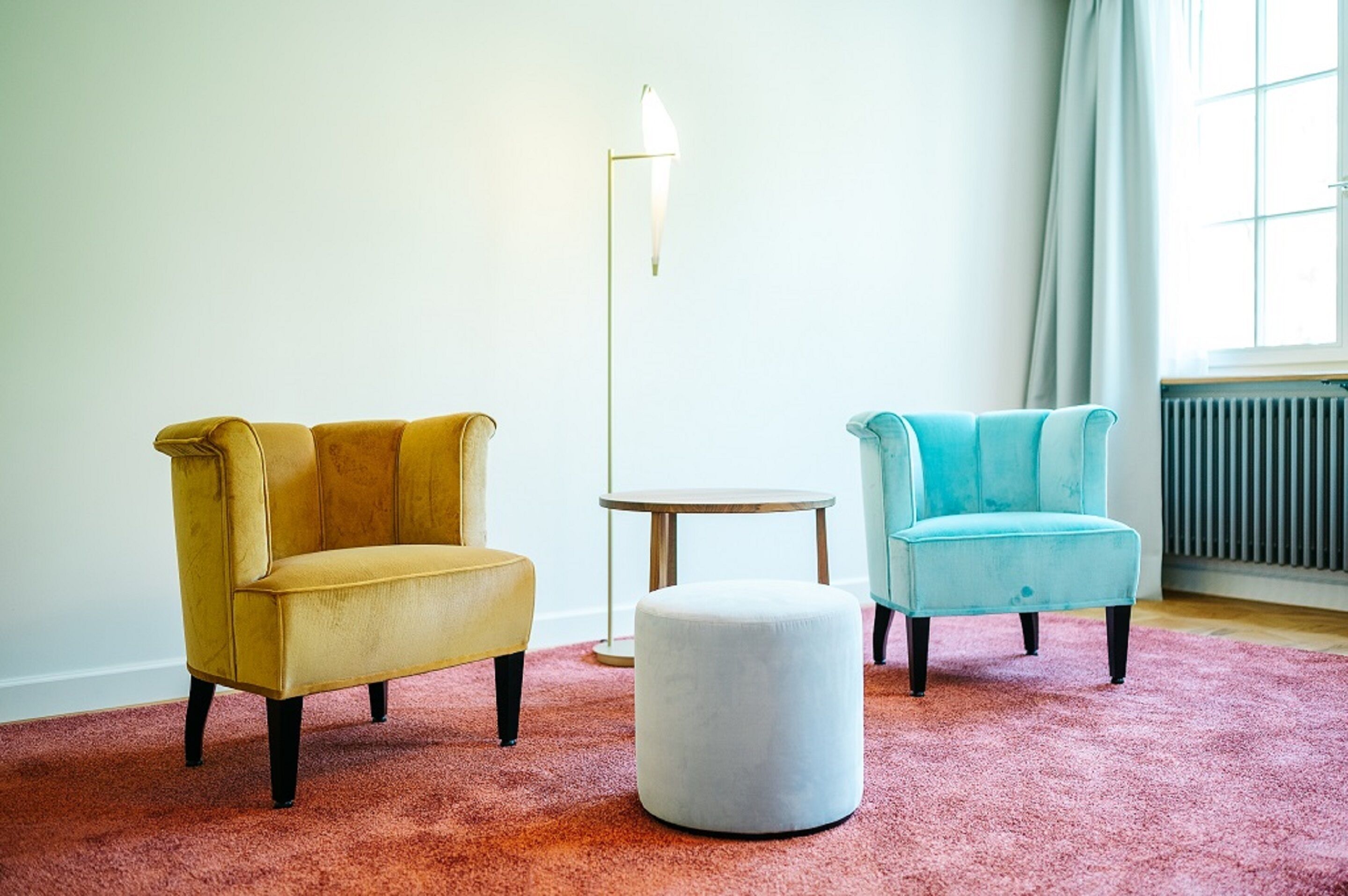A room with two armchairs, a small round table, and a white ottoman on a pink carpet.