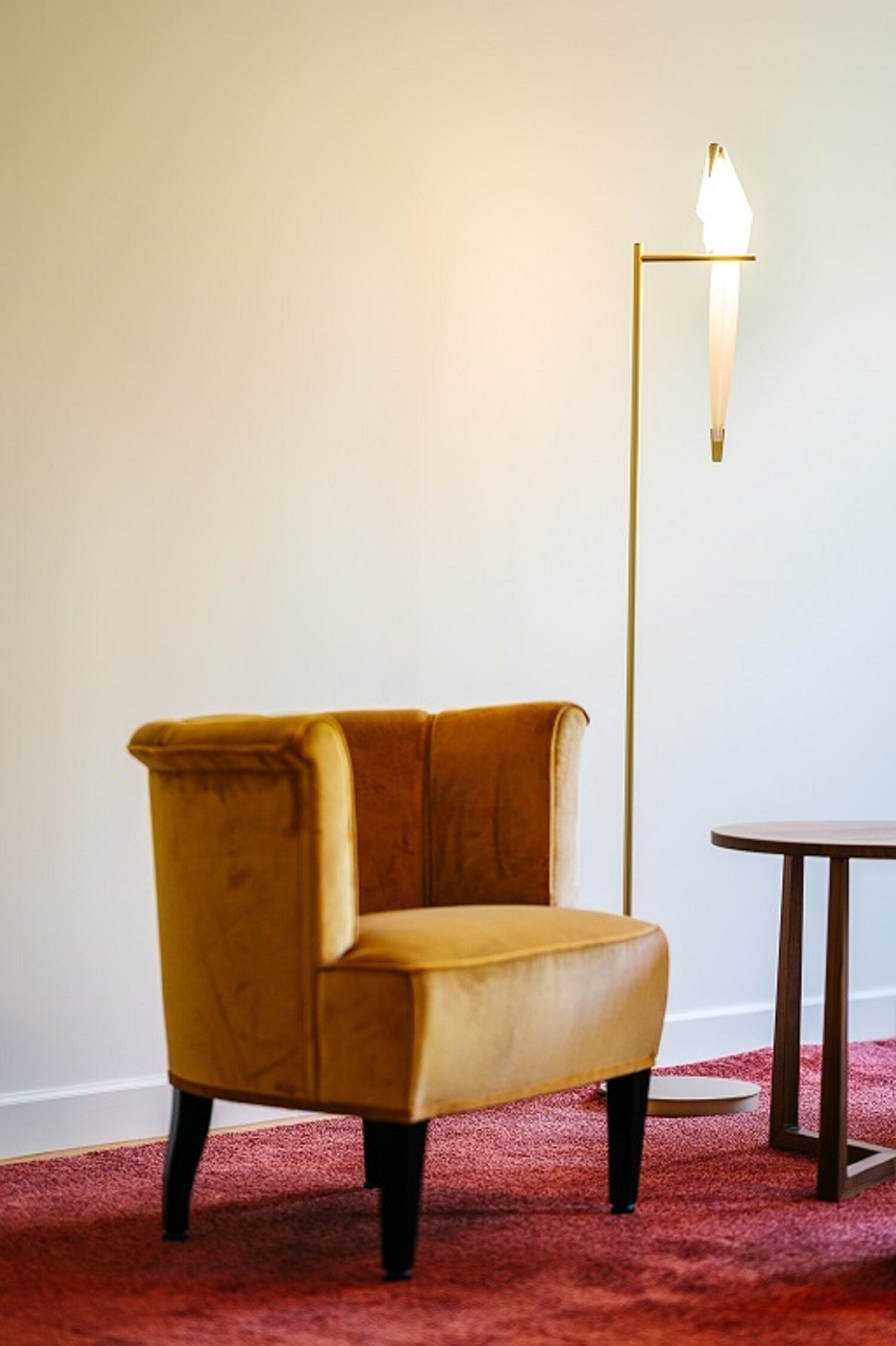A room with a mustard-colored armchair, a small round table, and a tall floor lamp.