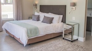 A bedroom with a bed, bedside lamps, a nightstand, and a view of the bathroom. - The Whale on Main B&B (Hermanus)