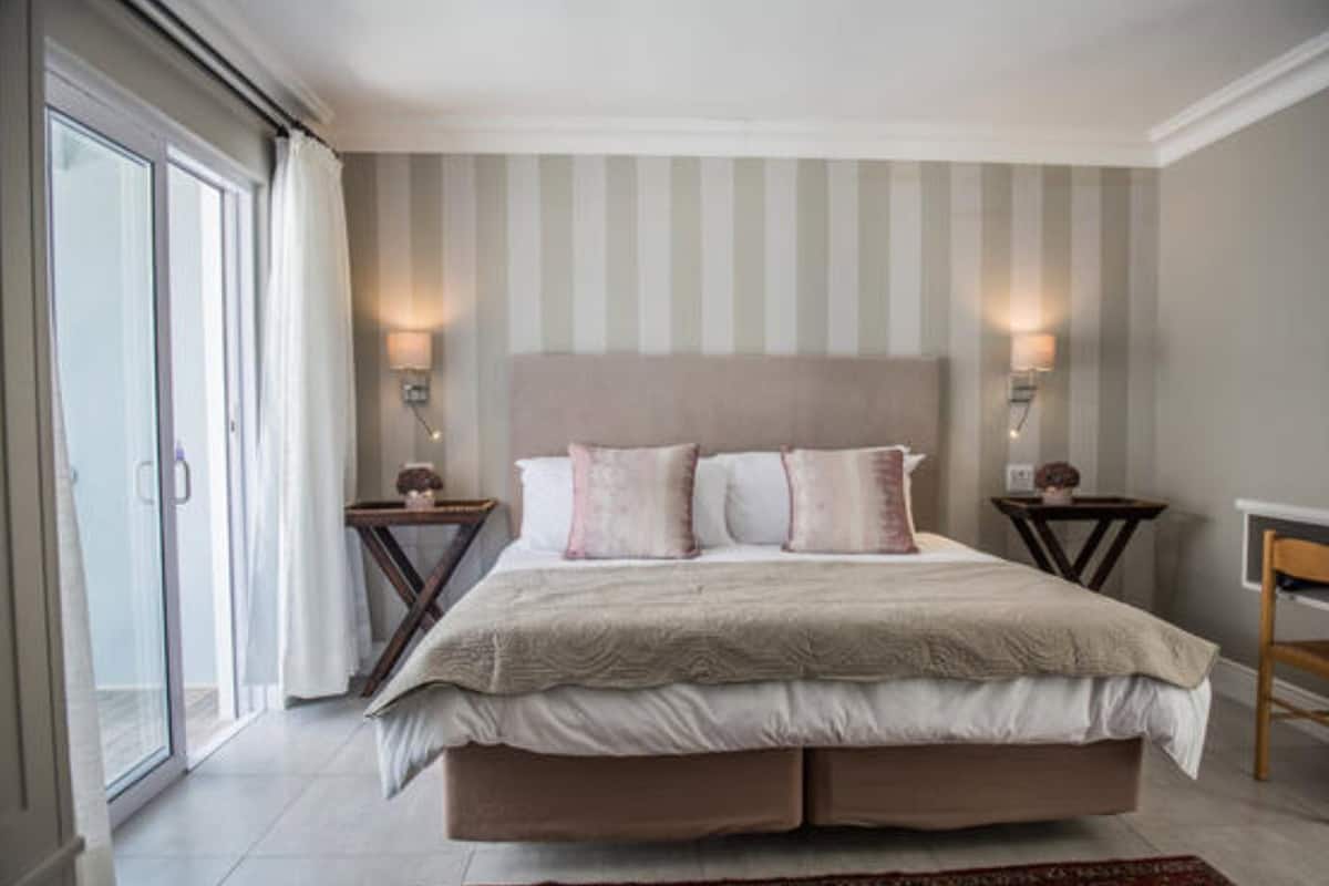 A bedroom with a large bed, two bedside tables, a chair, and a view of the outside through a sliding door.