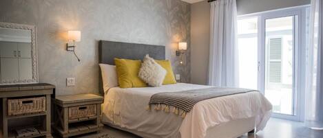 A bedroom with a bed, nightstands, a mirror, and a window with curtains.