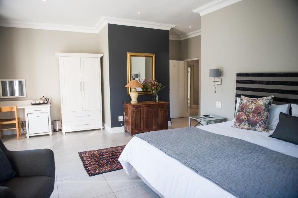 A bedroom with a bed, a desk, a wardrobe, a mirror, and a nightstand.