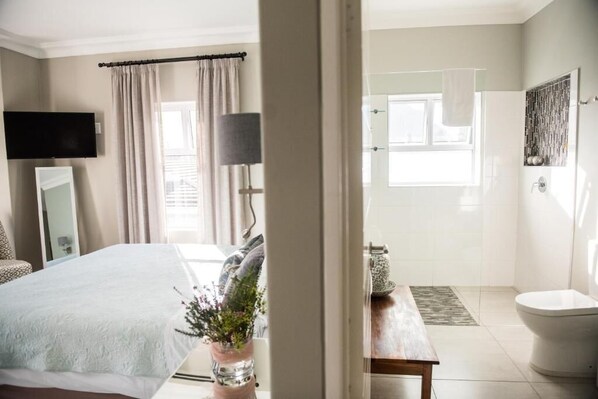 A bedroom with a bed, a bedside table, a lamp, a TV, and a window with curtains.