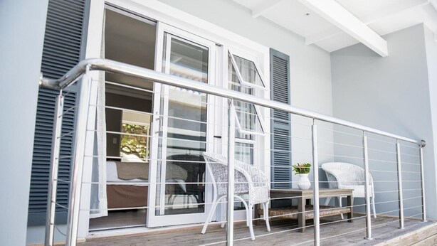A balcony with white wicker chairs and a small table, overlooking a garden. - The Whale on Main B&B (Hermanus)
