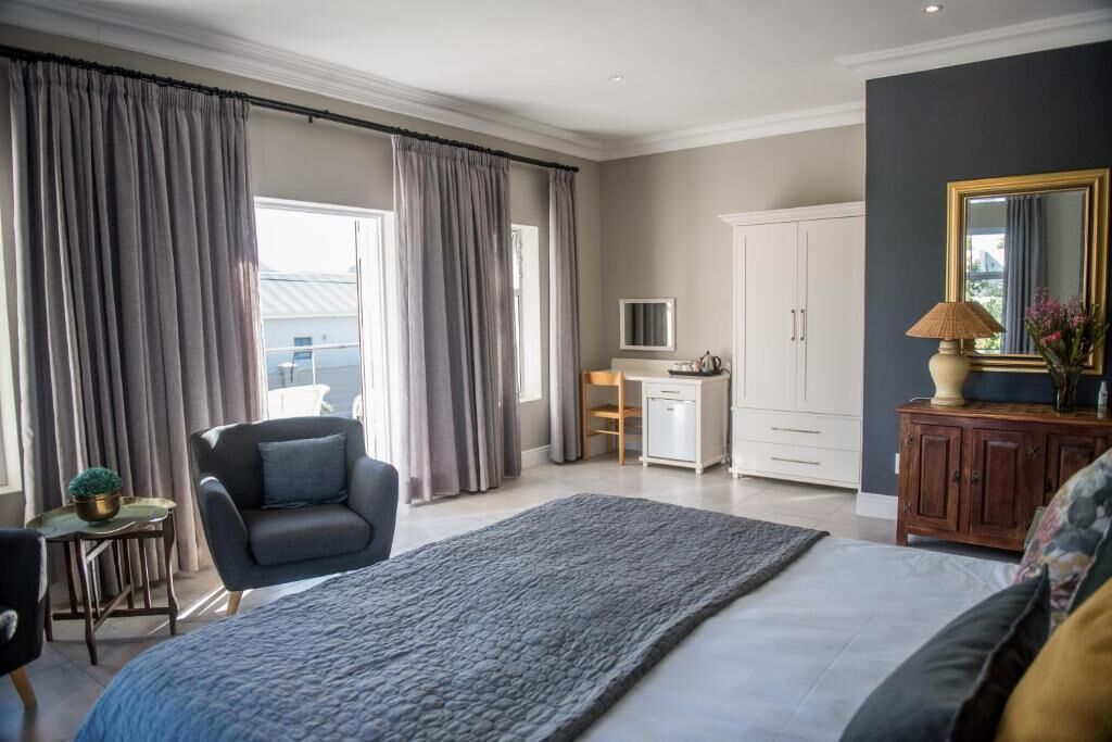 Habitación de hotel con cama, escritorio, silla, armario y un amplio ventanal con cortinas.
