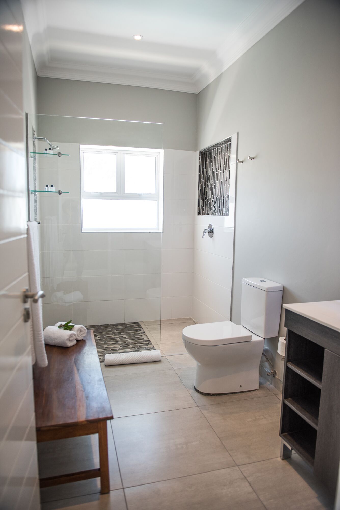Ein modernes Badezimmer mit Duschkabine aus Glas, Toilette und Holzbank.