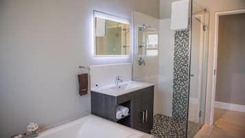 Un baño moderno con una bañera grande, un tocador con espejo y una zona de ducha con puerta de cristal.