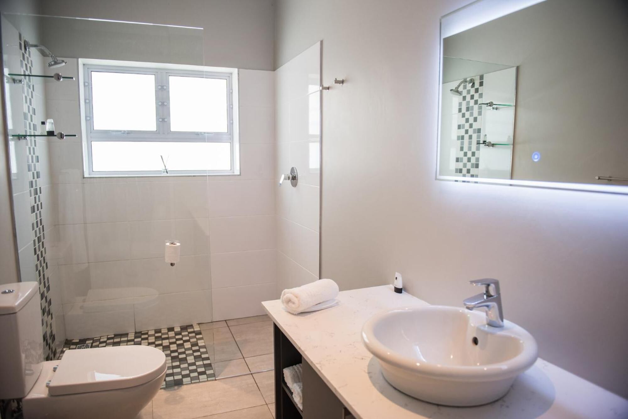 Un baño moderno con inodoro, lavabo, ducha y ventana.
