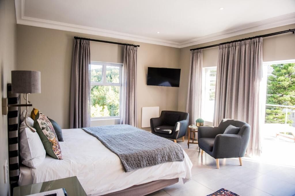 Un dormitorio moderno con una cama grande, dos sillones, un televisor y una ventana con cortinas.