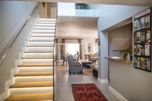 A staircase leading to a second floor, a dining area with chairs and a table, and a bulletin board with papers and magazines. - The Whale on Main B&B (Hermanus)