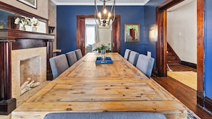 A long wooden dining table with grey upholstered chairs, a chandelier, and a fireplace. - Serene, Smart, Spacious. Near Downtown, In A Quiet Neighborhood (Pittsburgh)