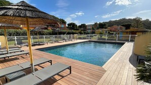 Ett trädäck med en swimmingpool, solstolar och ett parasoll med halmtak.