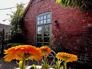 A red brick building with a green door and windows, surrounded by plants and flowers. - Idyllic riverside location (Hereford)