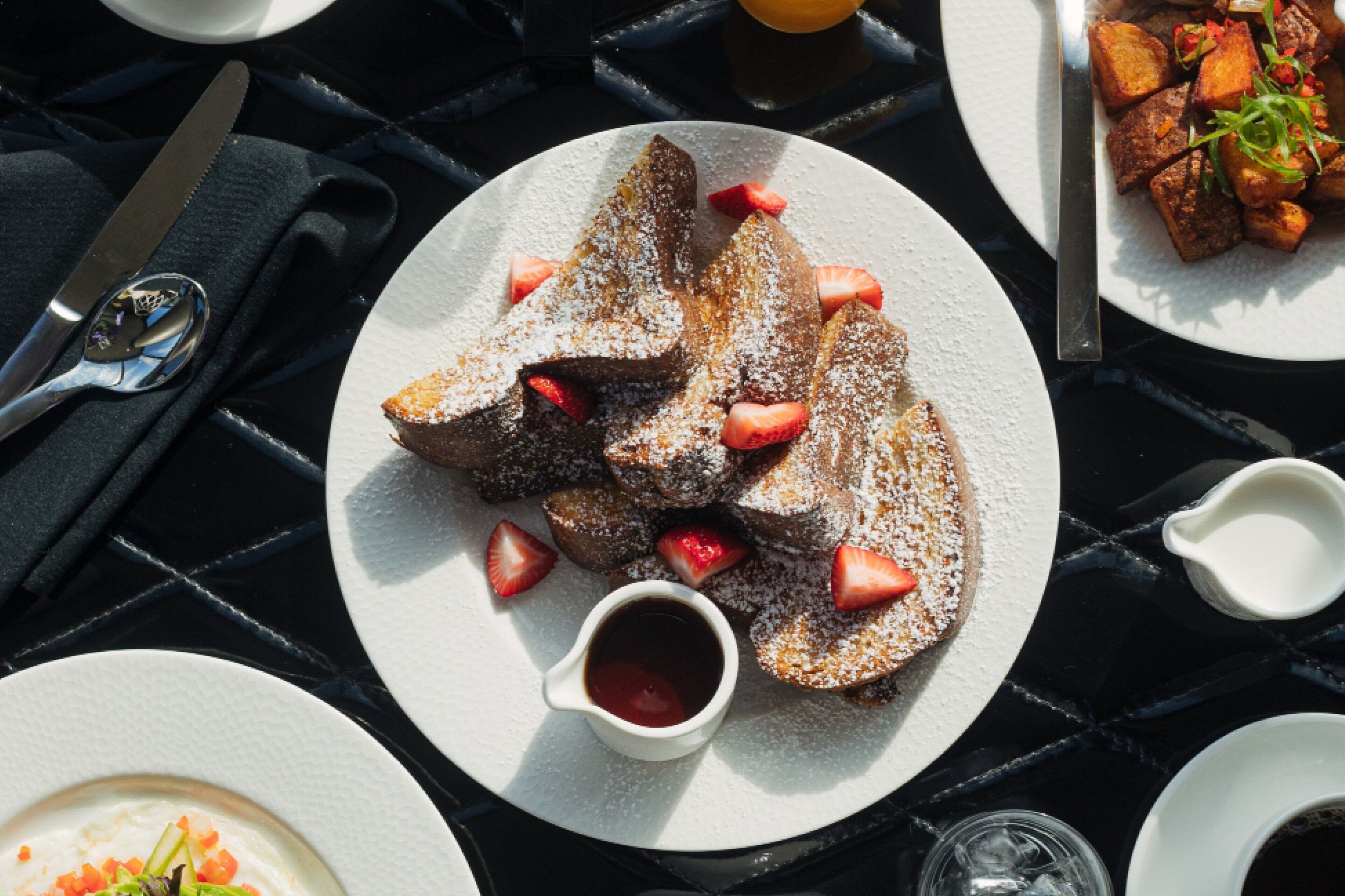 A breakfast setting with a plate of French toast, strawberries, and powdered sugar.