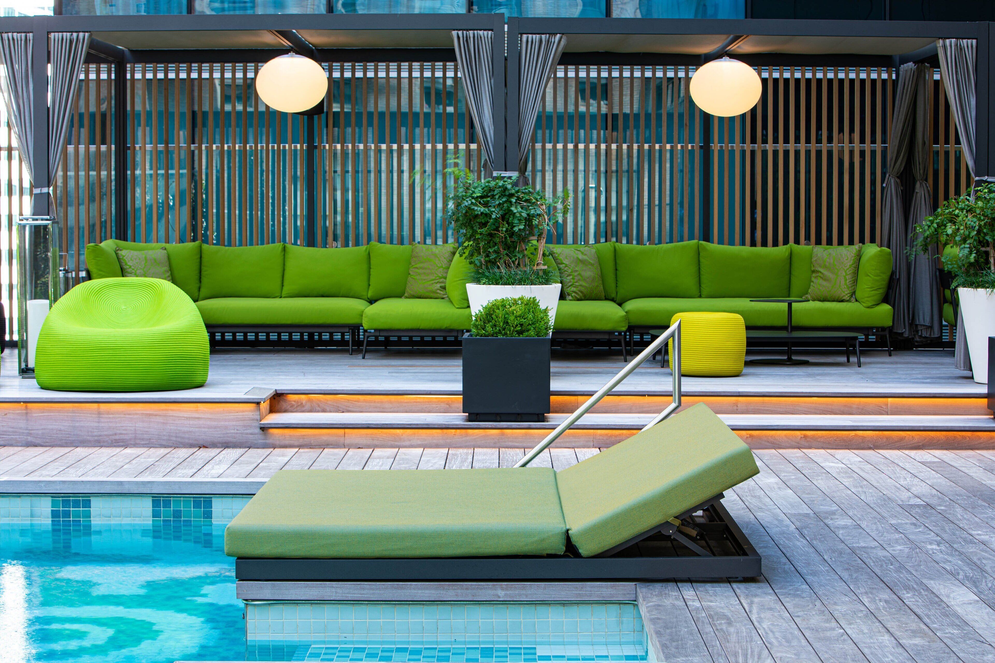 A poolside area with a green sofa, a yellow lounge chair, and a potted plant.