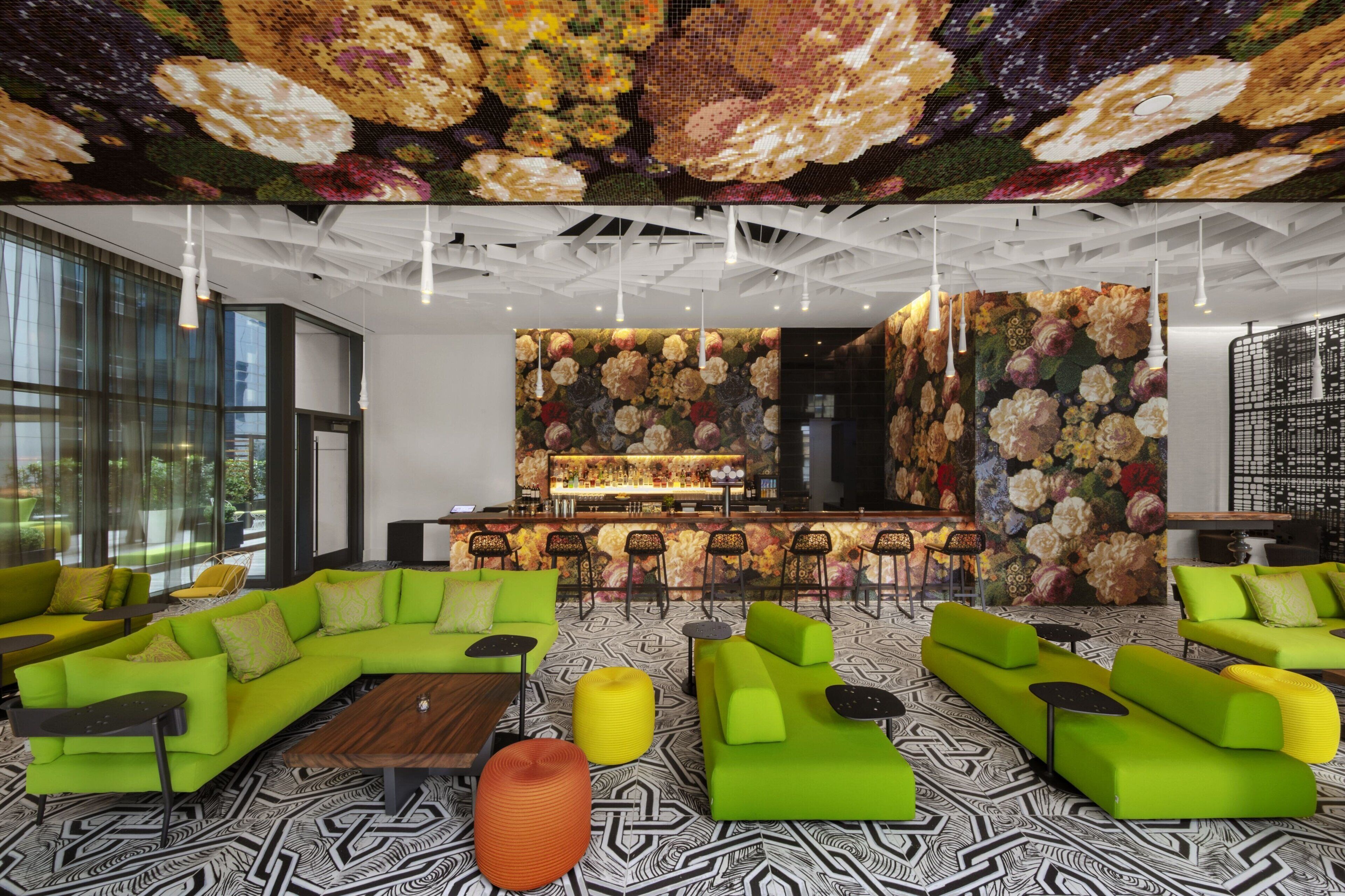 A modern lounge area with green sofas, a bar, and a patterned floor.