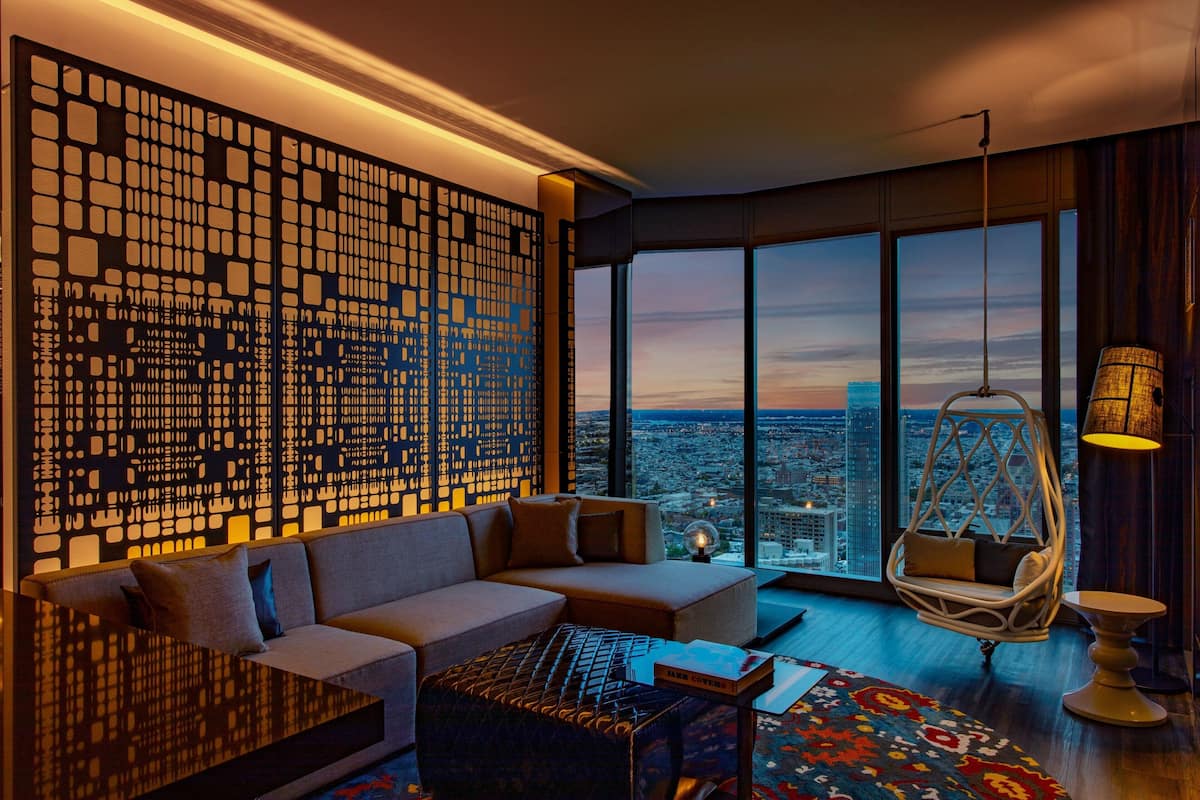 A modern living room with a large window, a decorative wall panel, a sofa, a hanging chair, and a coffee table.