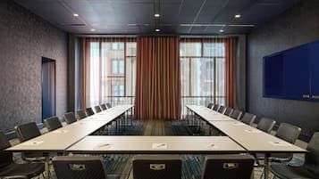 Sala de conferência com uma mesa comprida, cadeiras e uma janela grande com cortinas.