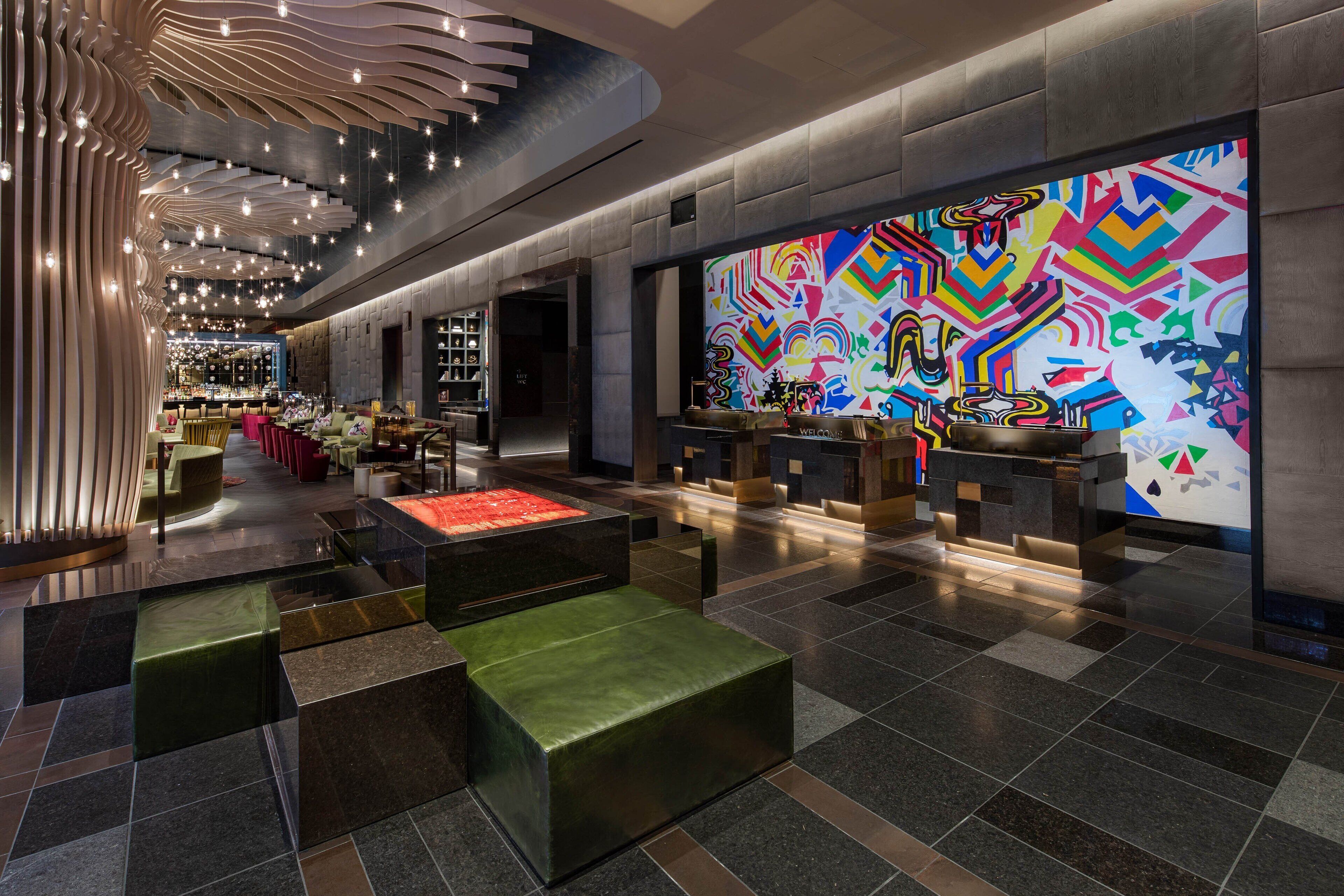A modern hotel lobby with a bar area, seating, and a colorful abstract mural.