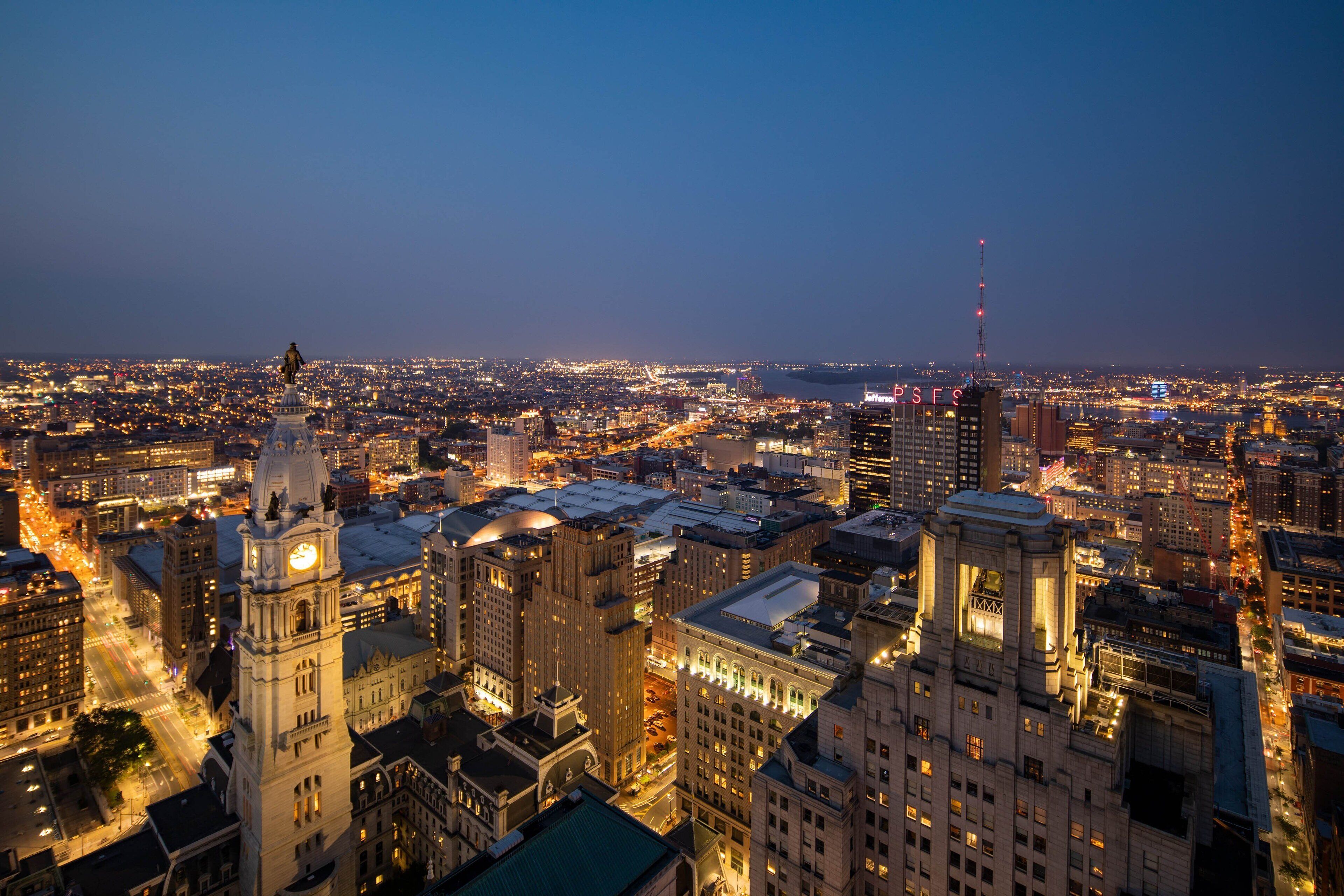 A cityscape at dusk with illuminated buildings and a prominent clock tower.