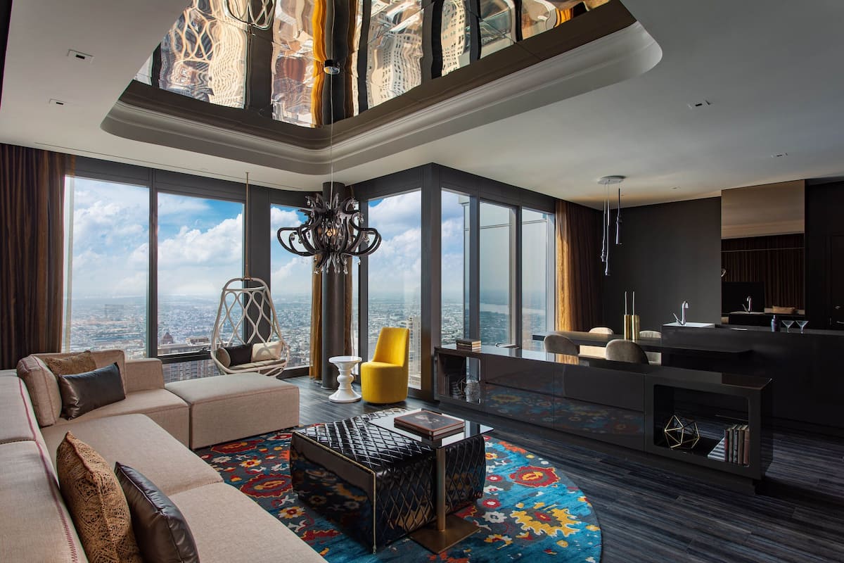 A spacious living area with a large window offering a city view, a modern sofa, a yellow chair, and a unique coffee table.