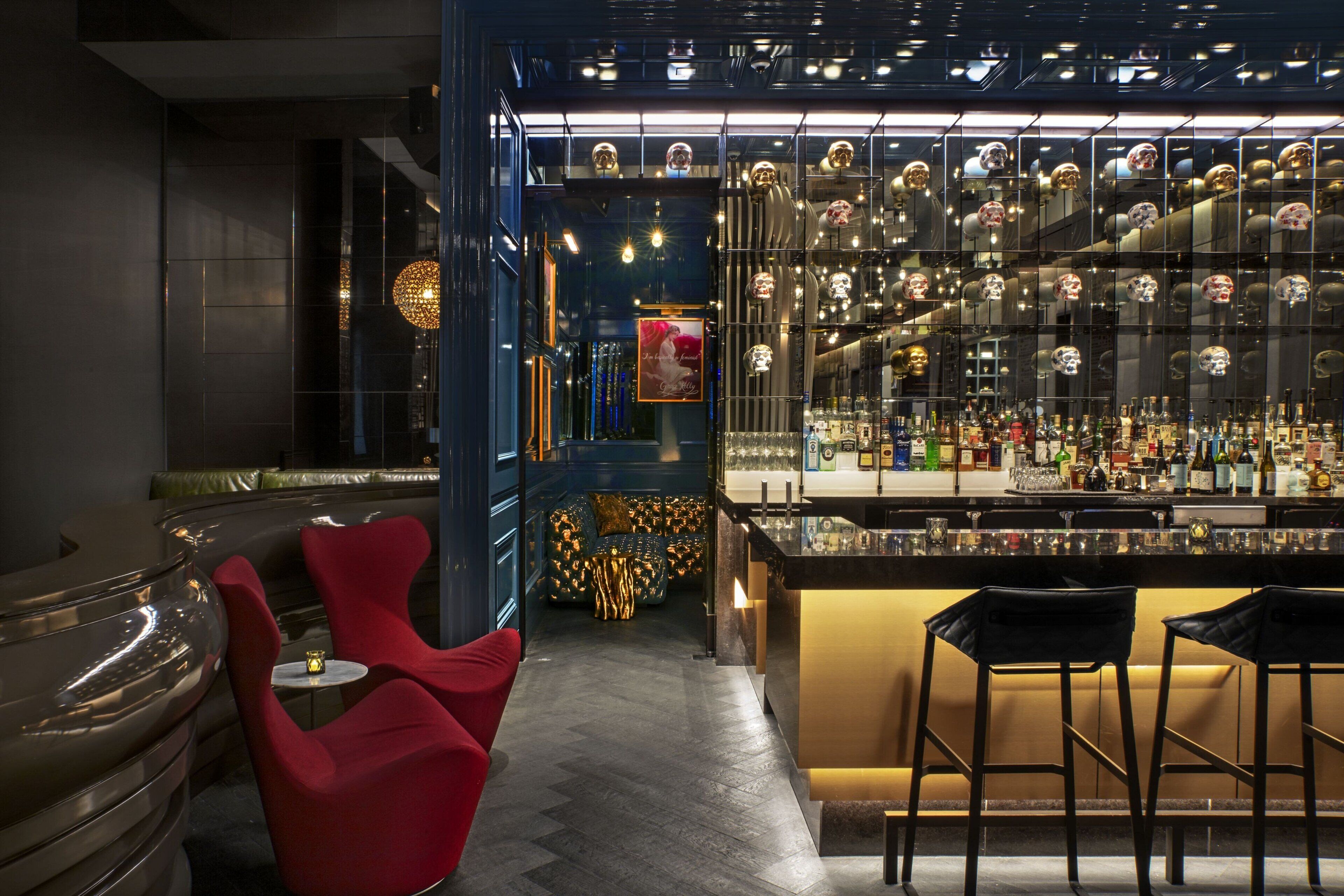 Un espace bar moderne comprenant un comptoir, des tabourets et un coin salon avec des chaises rouges.