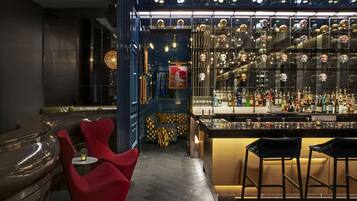 A modern bar area with a bar counter, stools, and a seating area with red chairs.