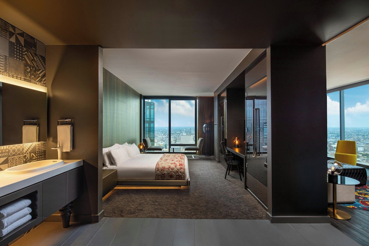 A modern hotel room with a large bed, a desk, and a view of the city.